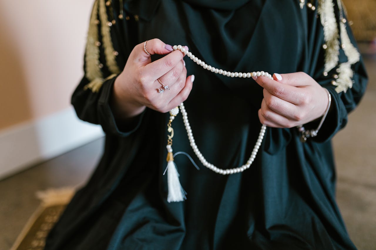 Close-up of a Muslim woman holding tasbih beads in prayer, symbolizing faith and spirituality.
