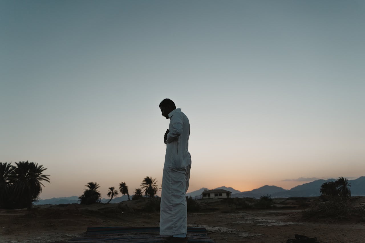 Services Silhouette of a man in traditional clothing praying outdoors at dawn.